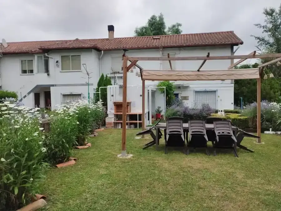 Casa blanca con techo de terracota, juego de comedor al aire libre y jardín con flores.