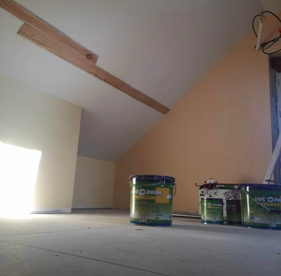 Prise de vue intérieure d'un grenier en construction ; des pots de peinture sont posés sur le sol avec la lumière provenant d'une fenêtre lumineuse.