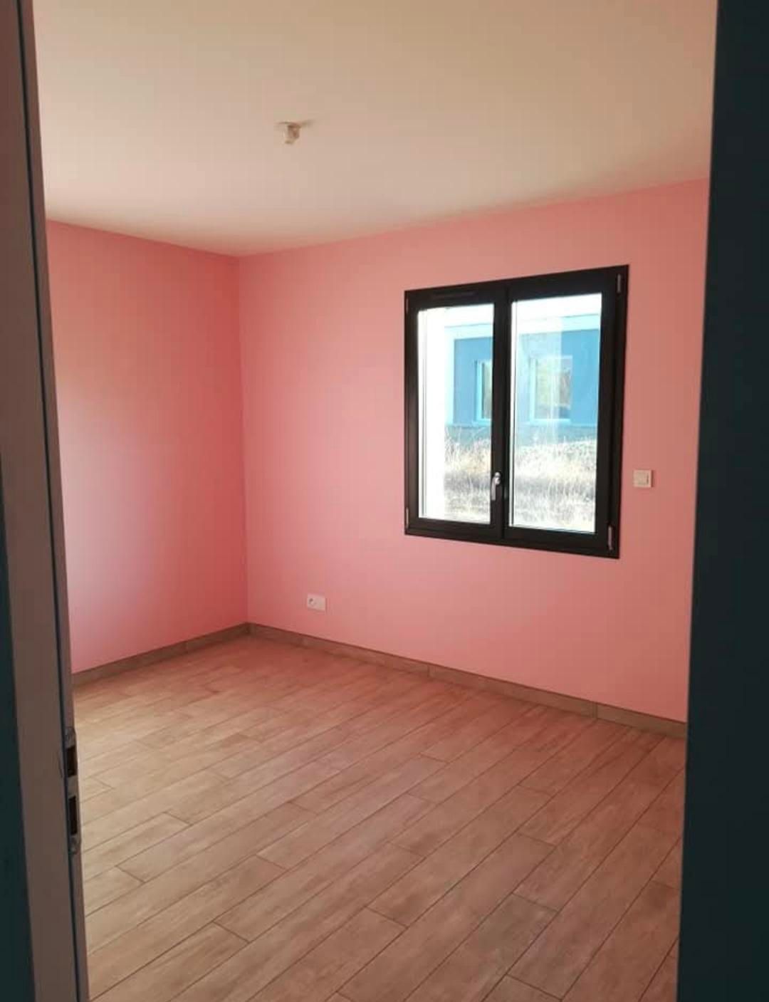 Pièce vide avec murs roses, parquet, cadre de fenêtre sombre et plafond blanc.