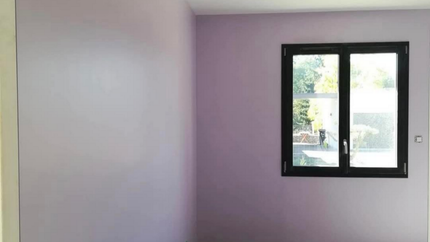 Pièce vide avec des murs lavande, une fenêtre à cadre noir et un aperçu du cadre de la porte.