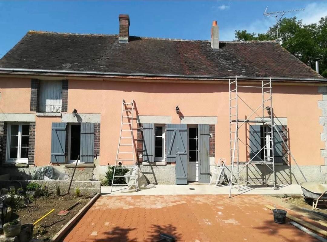 Maison couleur pêche aux volets et au toit gris, en construction. Échelle et échafaudage en façade.