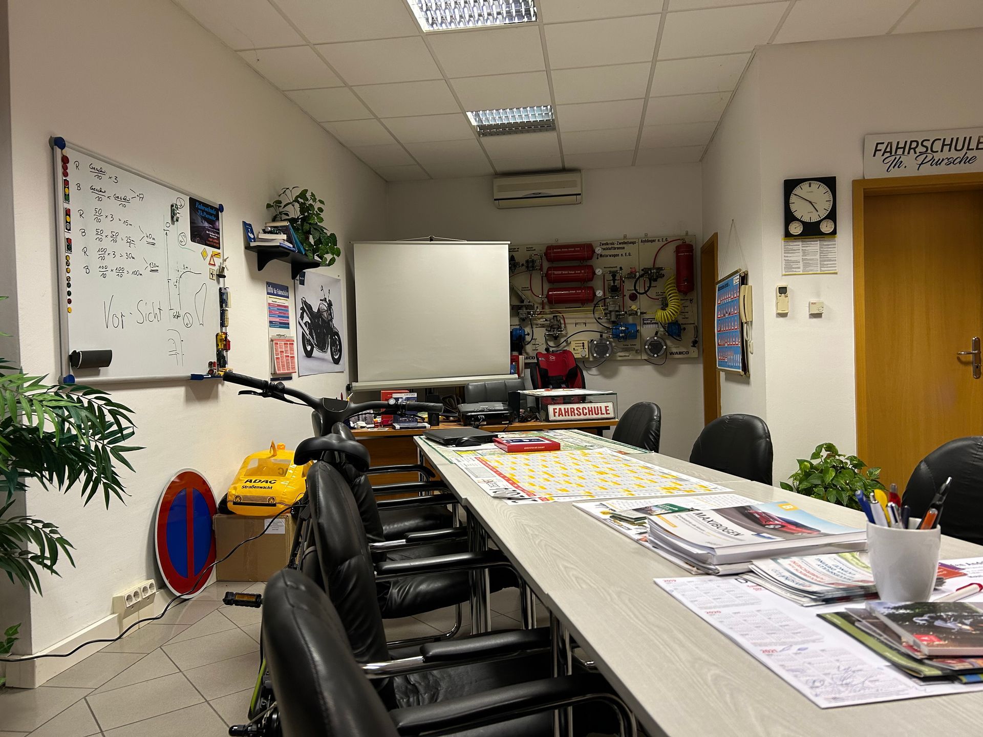 Ein Klassenzimmer mit einem langen Tisch, Stühlen, einer Tafel und Verkehrsschildern.