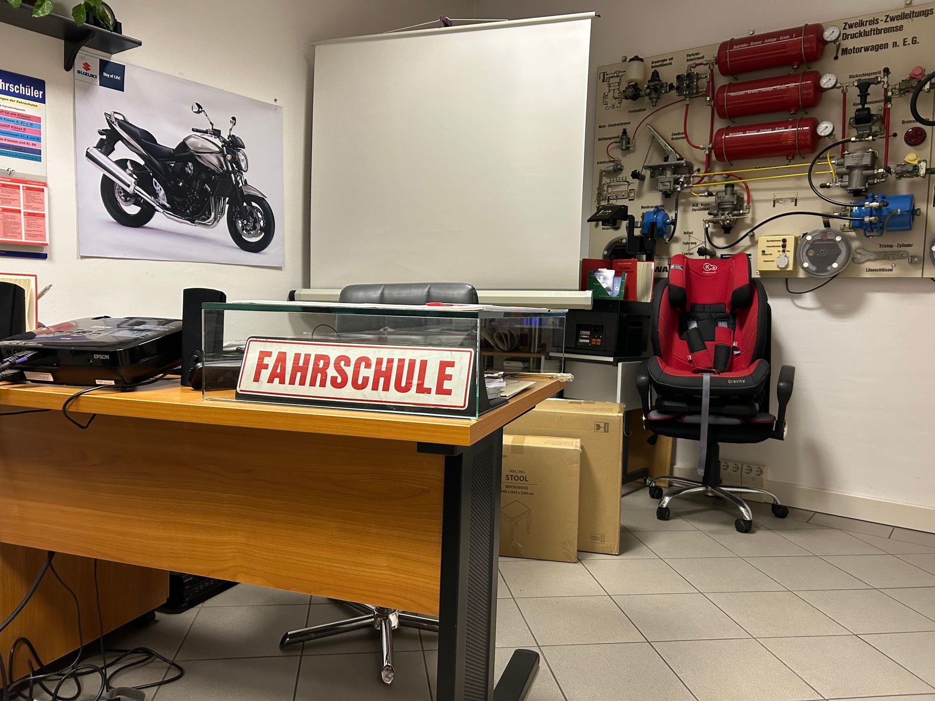 Ein Fahrschulbüro mit Schreibtisch, Motorradposter und Lehrmitteln an der Wand.