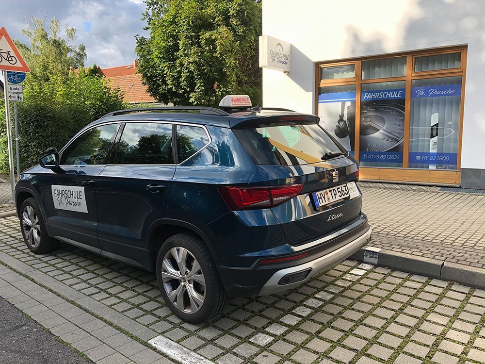 Ein blaues Taxi parkt neben einem Gebäude mit Schaufenster. Auf dem Dach prangt ein „Taxi“-Schild. Davor befindet sich ein Bürgersteig.