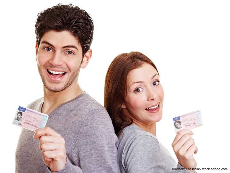 Mann und Frau, lächelnd, halten Ausweise in der Hand, stehen Rücken an Rücken vor einem weißen Hintergrund.