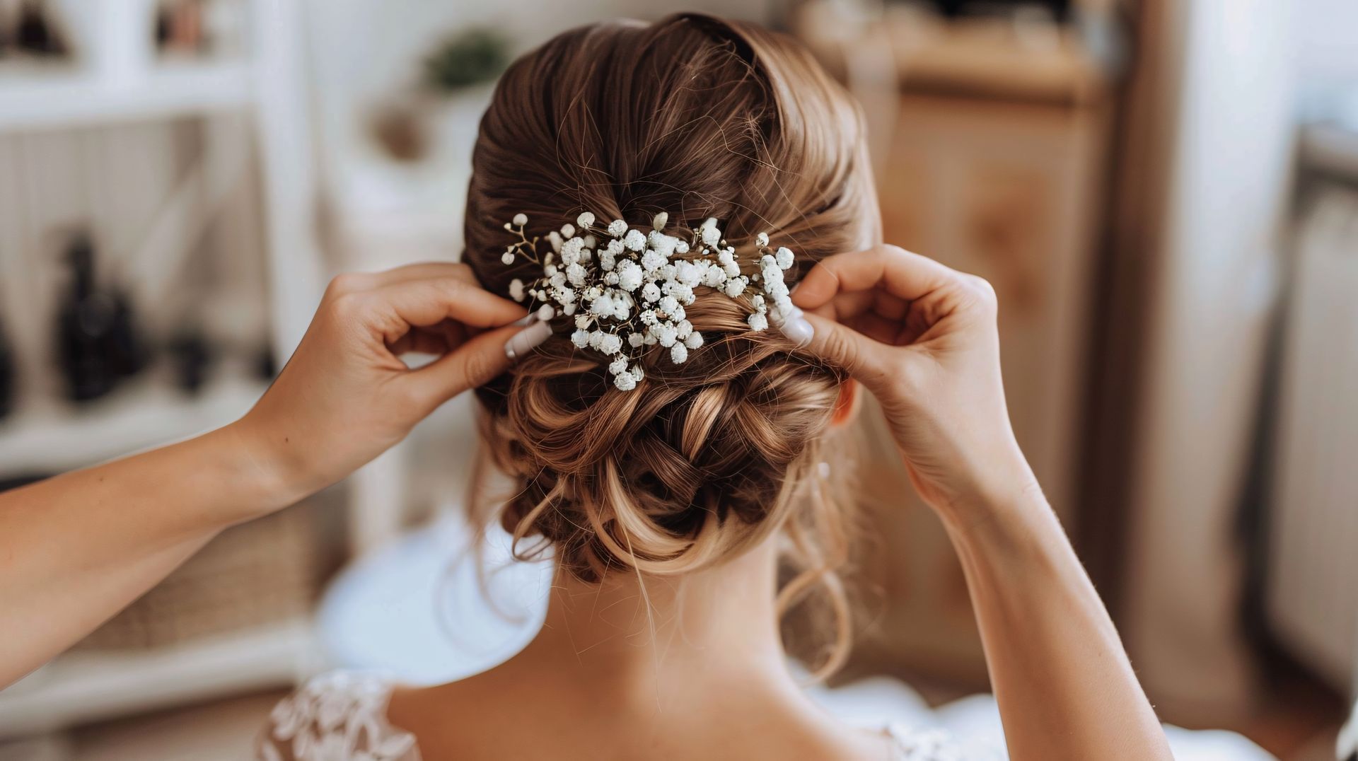 Une personne coiffe ses cheveux en un élégant chignon bas orné d'un brin de délicates fleurs blanches de gypsophiles.