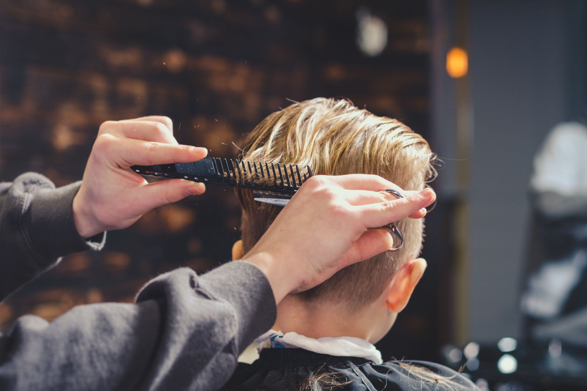 Dans un salon faiblement éclairé, une coiffeuse, munie d'un peigne et de ciseaux, coupe les cheveux humides d'une cliente.
