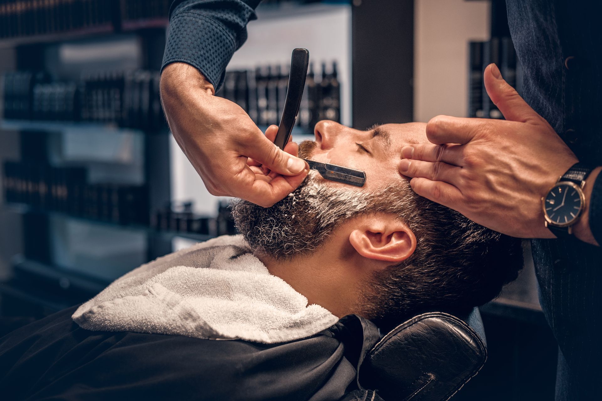 Dans un salon de coiffure, un barbier utilise un rasoir droit pour raser la barbe d'un client.