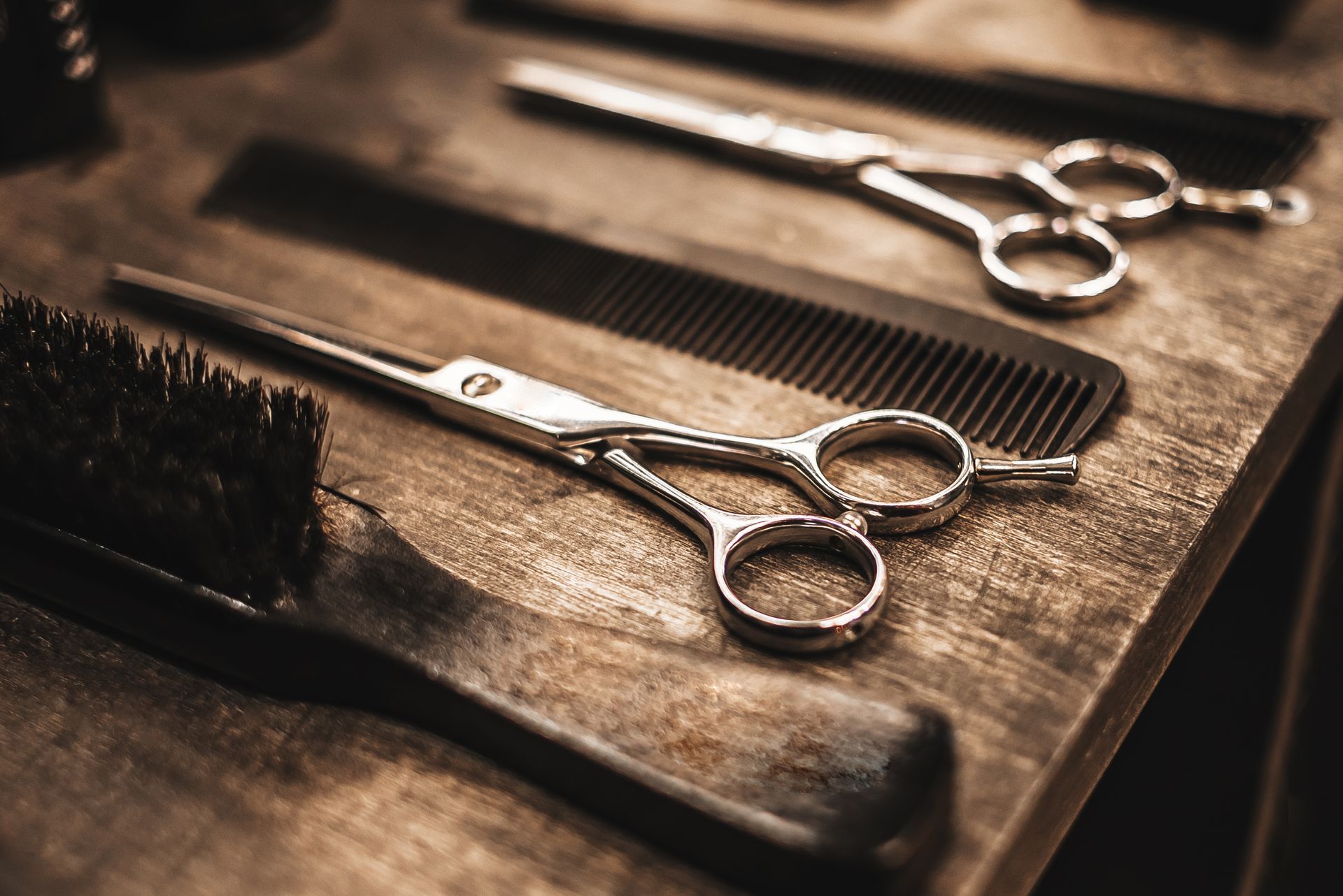 Des outils de coiffeur, notamment des ciseaux, un peigne et une brosse, sont soigneusement disposés sur une surface en bois sombre et rustique.