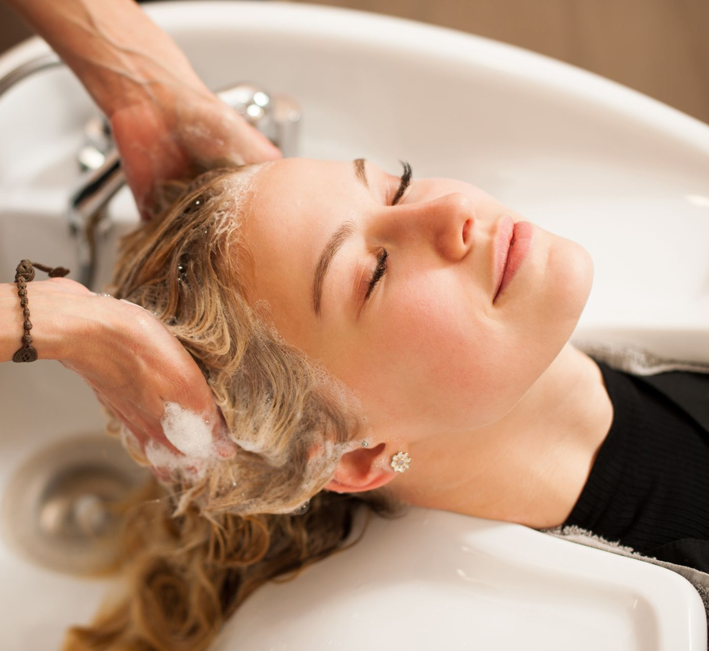 Une personne se fait laver les cheveux dans un lavabo de salon, avec du shampoing moussant massé sur les cheveux.
