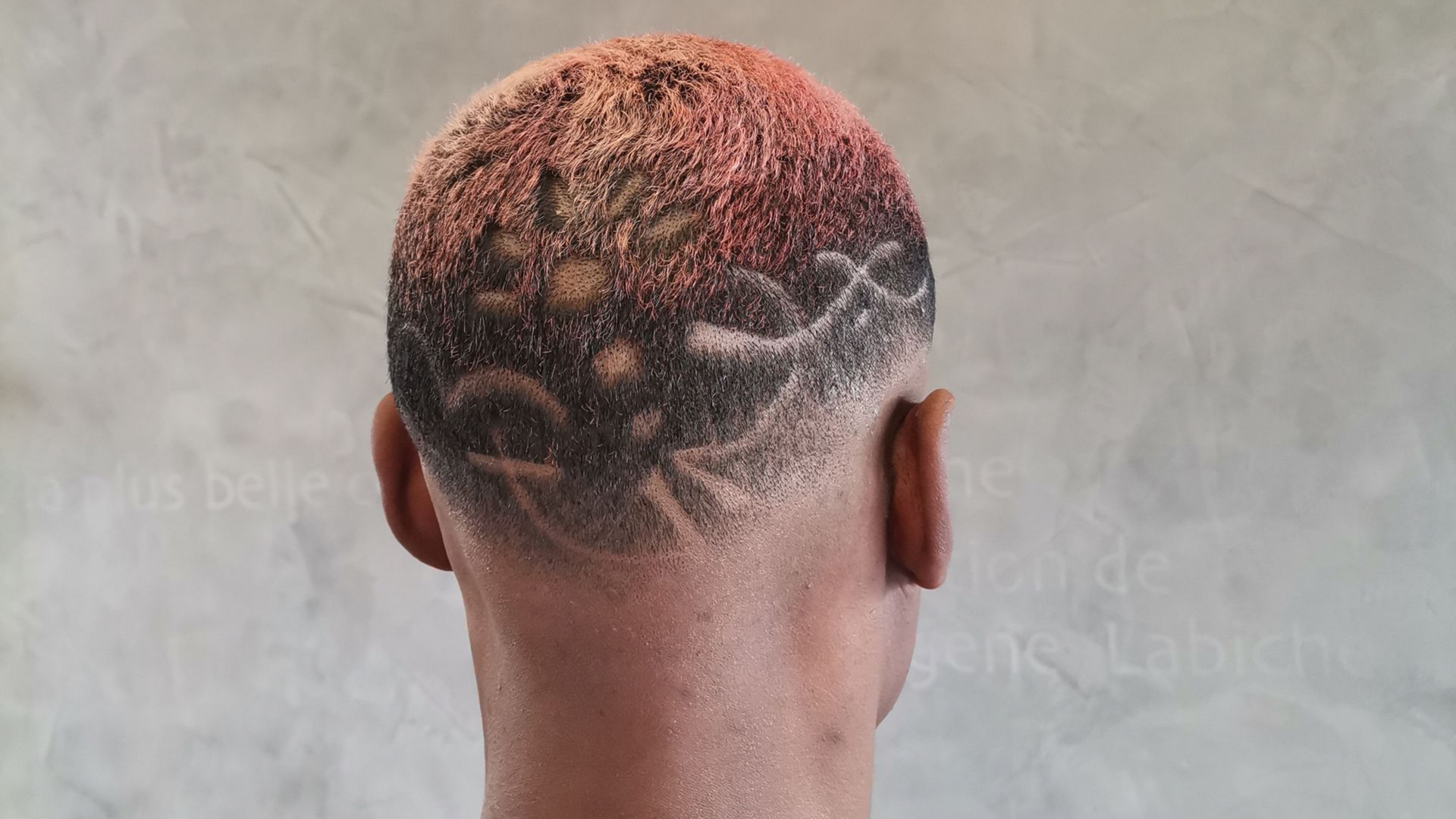 Vue arrière d'une coupe de cheveux très courte présentant un motif tribal stylisé rasé et un dégradé de cheveux roses et brun foncé.