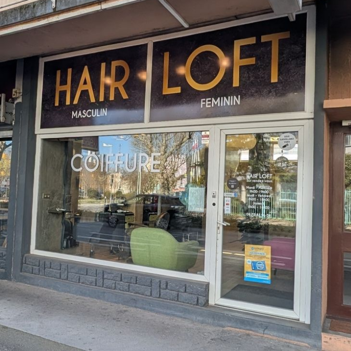 Vue au niveau de la rue de la façade d'un salon de coiffure appelé Hair Loft, avec de grandes fenêtres et une porte vitrée.