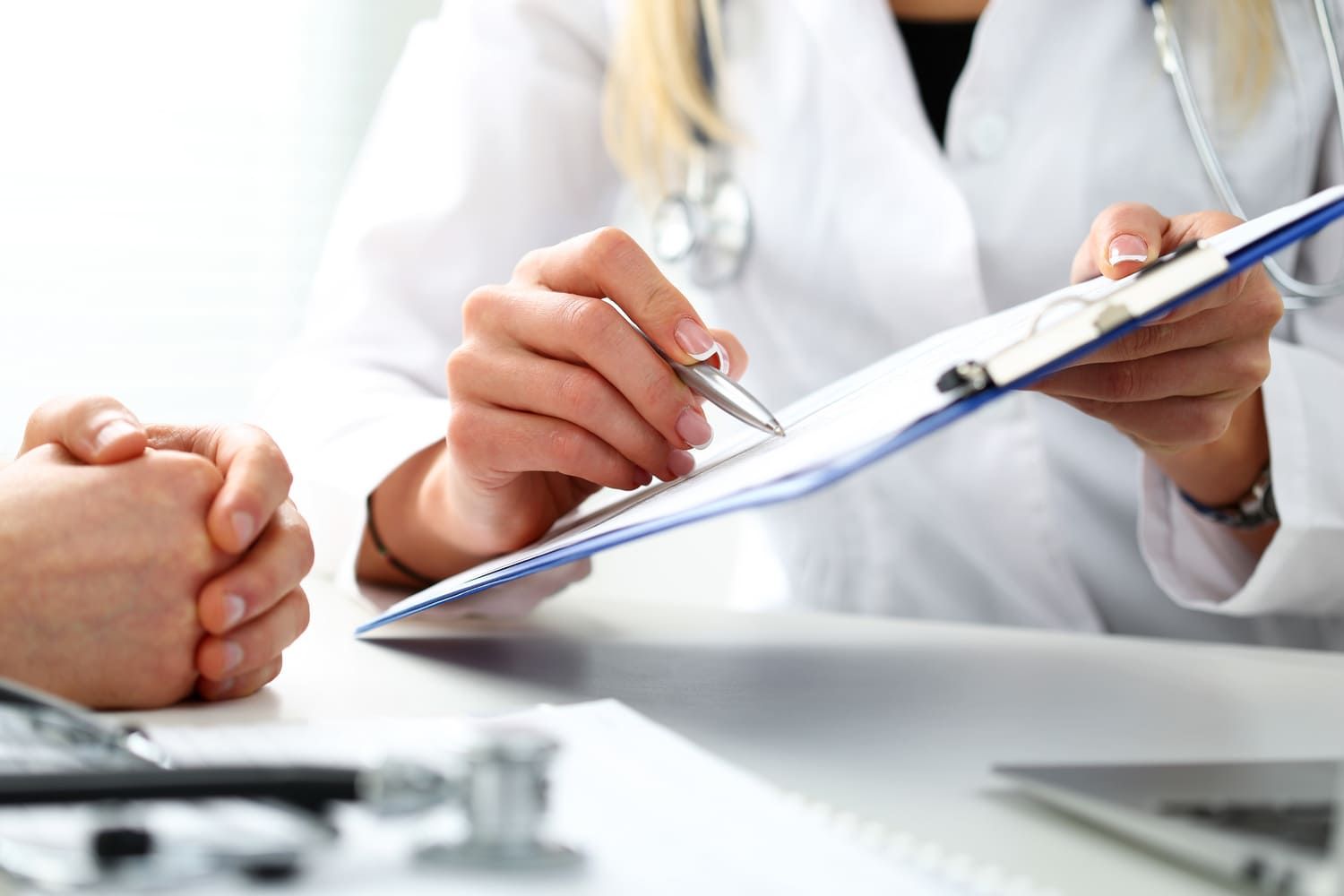 Un médico sostiene un portapapeles y habla con un paciente.