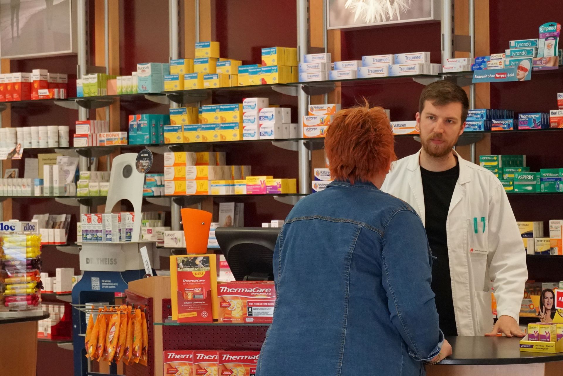 Apotheke mit einem Apotheker, der einen Kunden bedient. Regale voller Medikamente.