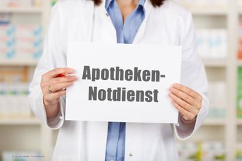 Ein Apotheker hält ein Schild mit der Aufschrift „Apotheken-Notdienst“.