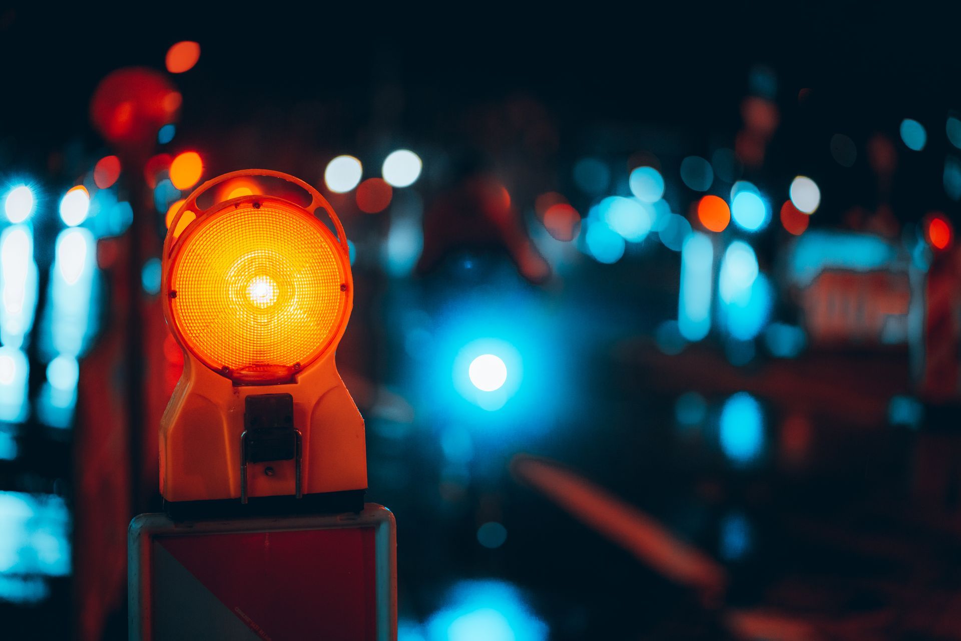 Feu de circulation orange vif dans une rue pluvieuse d'une ville la nuit, avec des lumières bleues floues (effet bokeh).