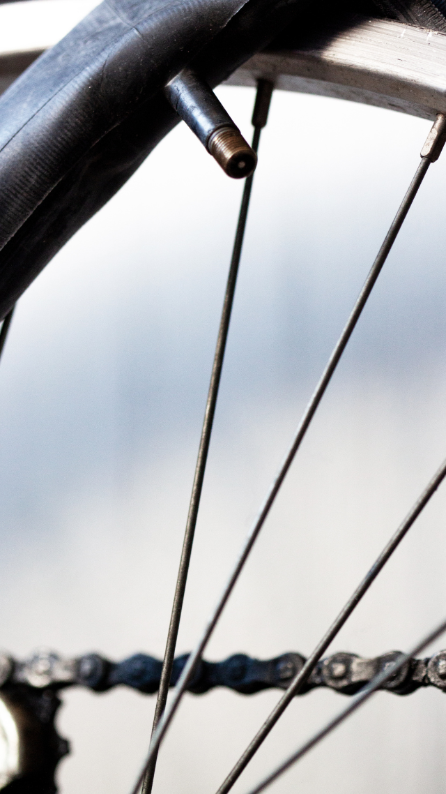 Gros plan d'une roue de vélo montrant la valve du pneu, les rayons et la chaîne sur un arrière-plan flou.