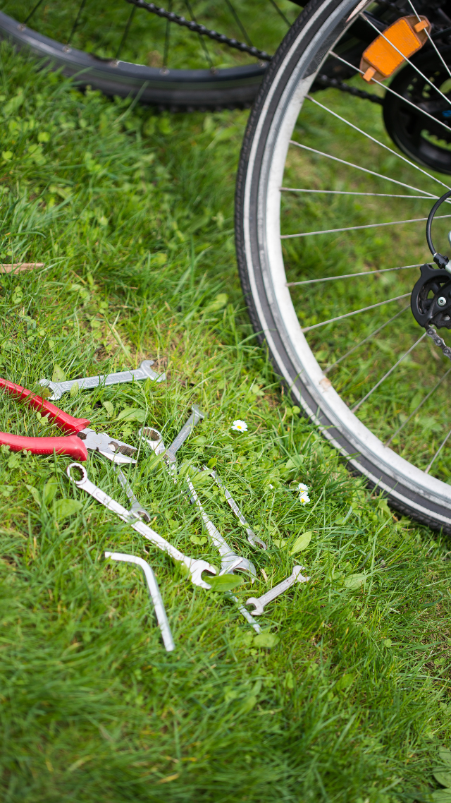 Roue de vélo avec outils sur l'herbe : pinces, clés, clés Allen, probablement pour des réparations.