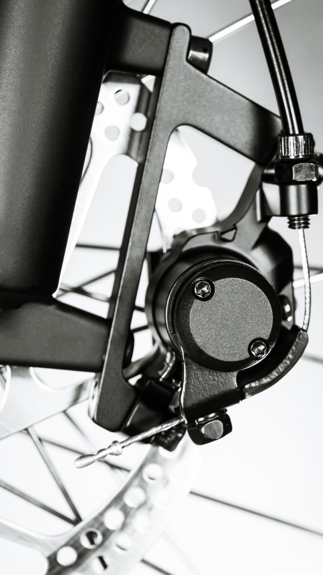 Gros plan noir et blanc d'un frein à disque de vélo, montrant l'étrier, le rotor et le support de montage.