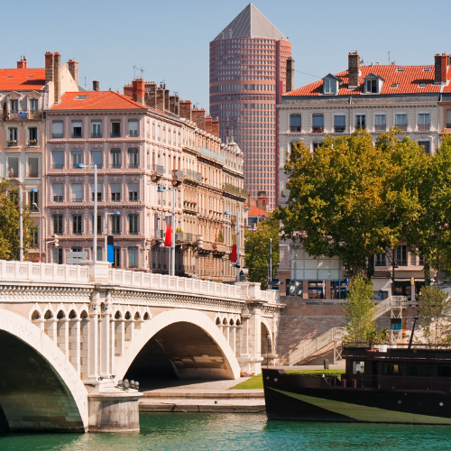 Pont sur la rivière à Lyon, en France, avec des bâtiments historiques et un gratte-ciel moderne.