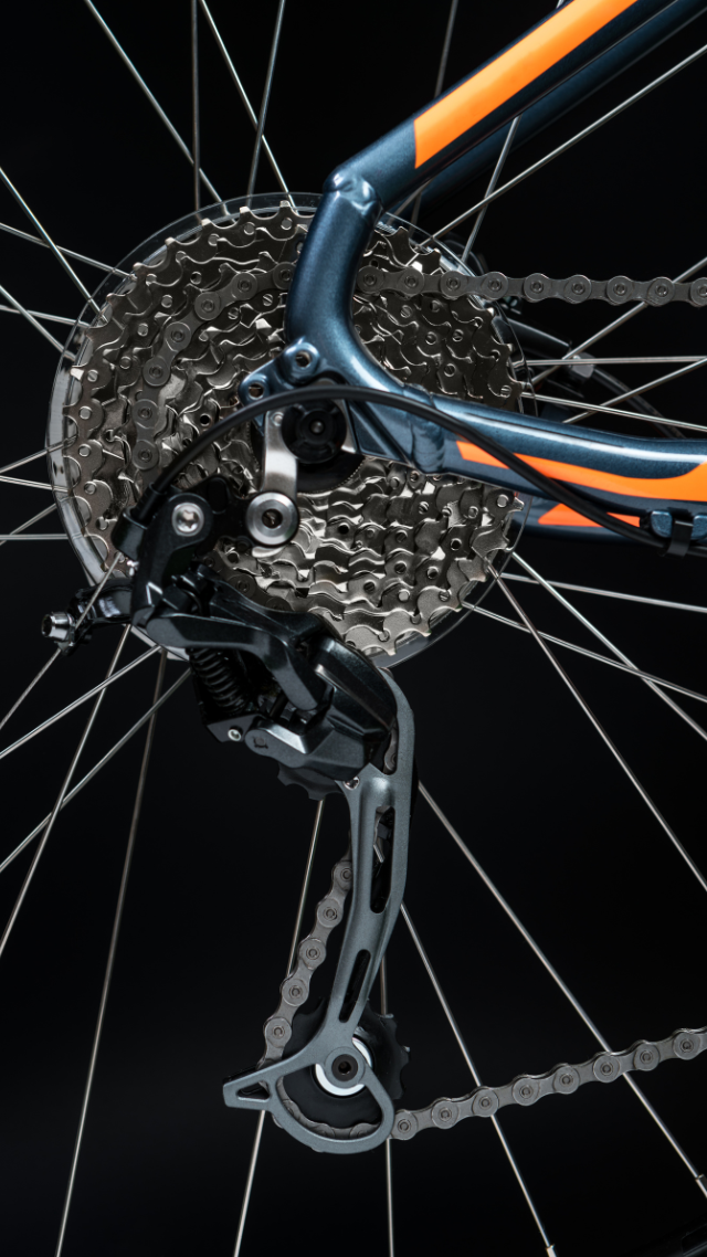 Roue arrière de vélo avec vitesses, dérailleur et chaîne sur fond sombre ; cadre bleu et orange.
