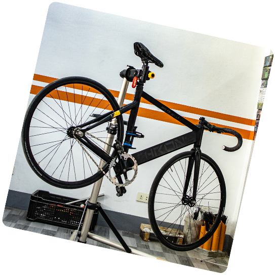 Vélo à pignon fixe noir sur un support de réparation, à l'intérieur avec un mur blanc et orange.