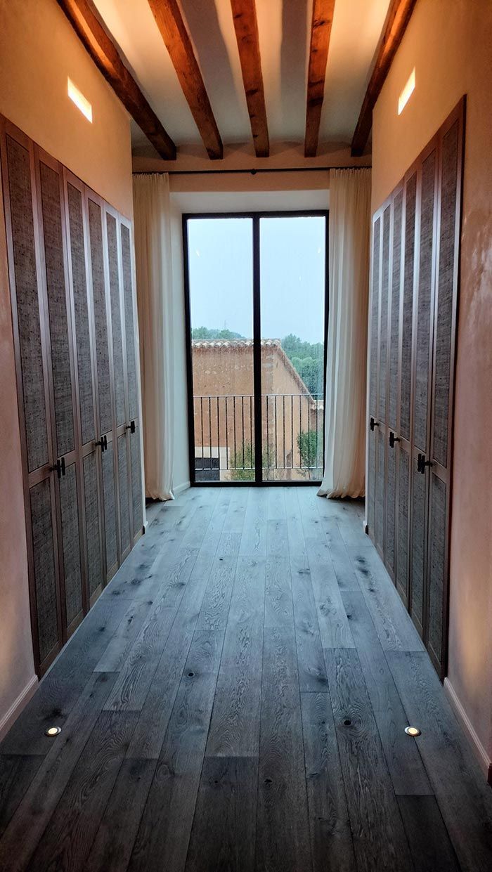 Pasillo con piso de madera, dos puertas de armario texturizadas, ventana y vigas a la vista en el techo.