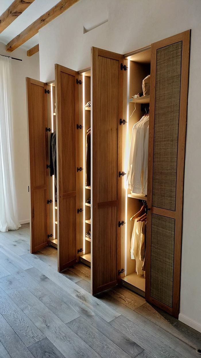 Armario de madera con múltiples puertas que se abren dejando ver la ropa y luces incorporadas.