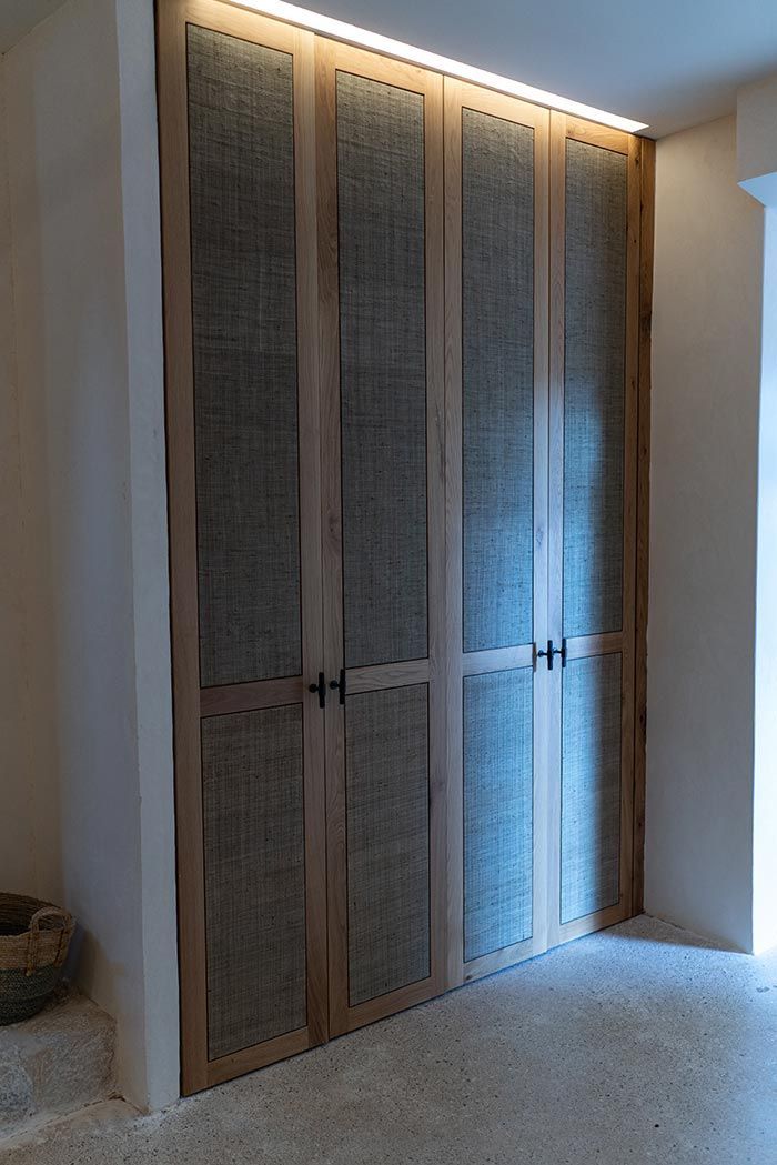 Puertas de armario de madera con inserciones de tela gris, iluminadas por luz cenital en una habitación de tonos neutros.