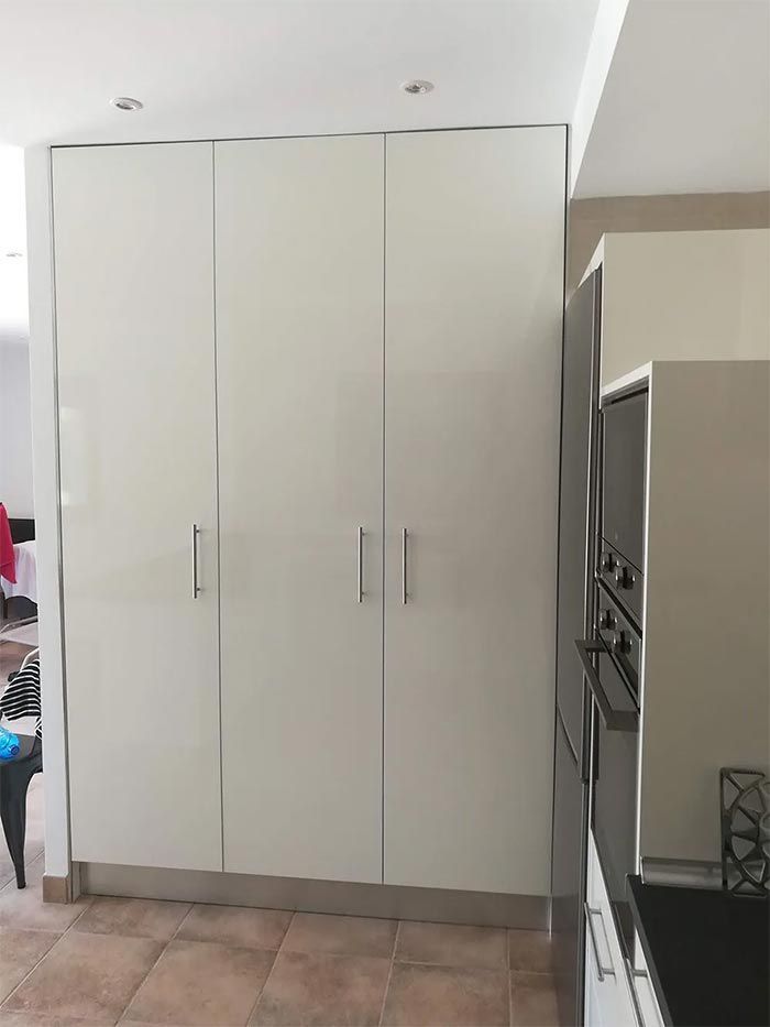 Muebles de despensa blancos en una cocina, junto a un horno empotrado y suelo de baldosas.