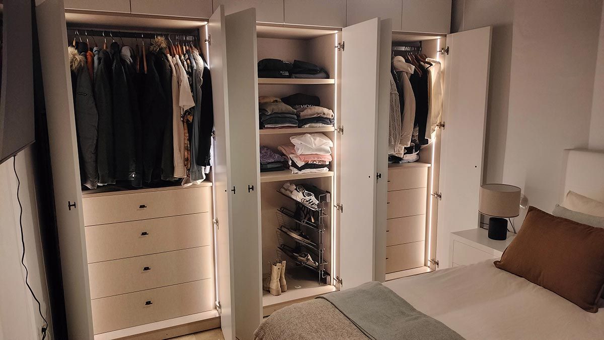Armario con puertas abiertas que dejan ver ropa y cajones. Una iluminación suave ilumina el interior.