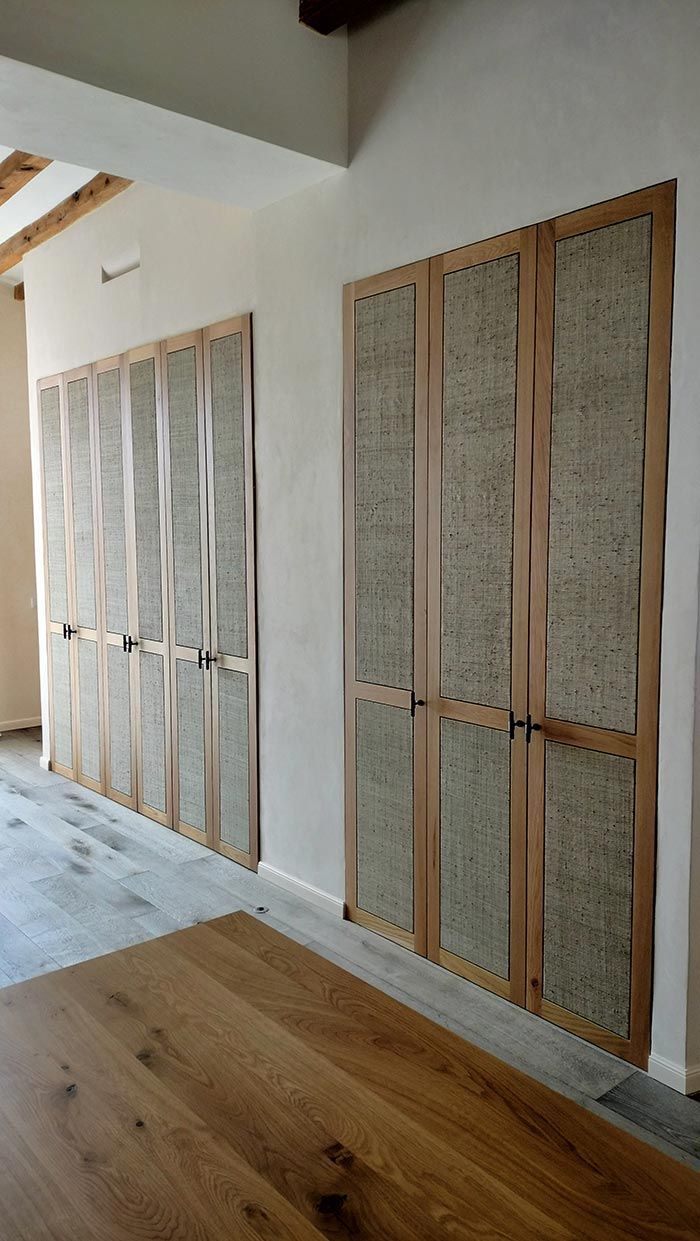 Dos puertas de madera con paneles texturizados, sobre una pared de color claro, con una mesa de madera en primer plano.