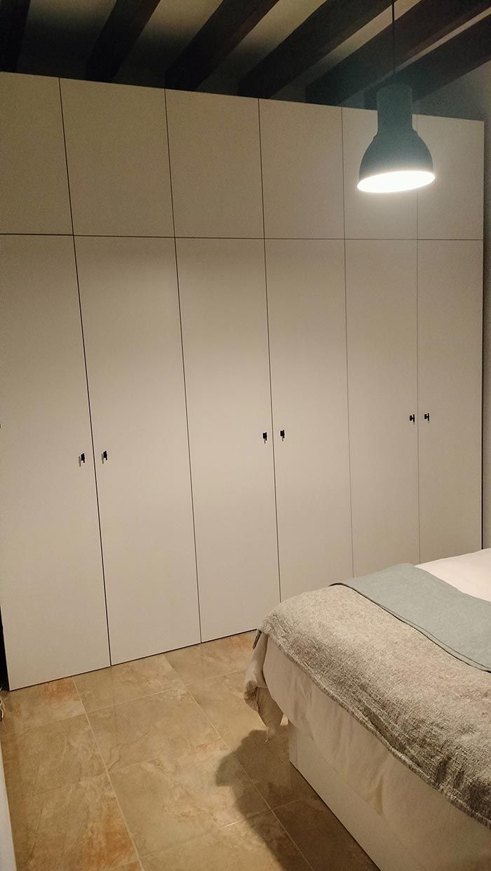 Un armario blanco contra la pared; se ve parcialmente una cama frente a él. Una lámpara cuelga del techo.