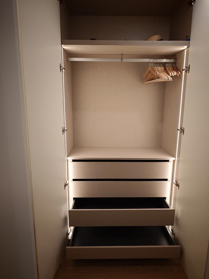 Armario vacío e iluminado con barra para colgar, estantes y cajones abiertos. Interior beige y negro.