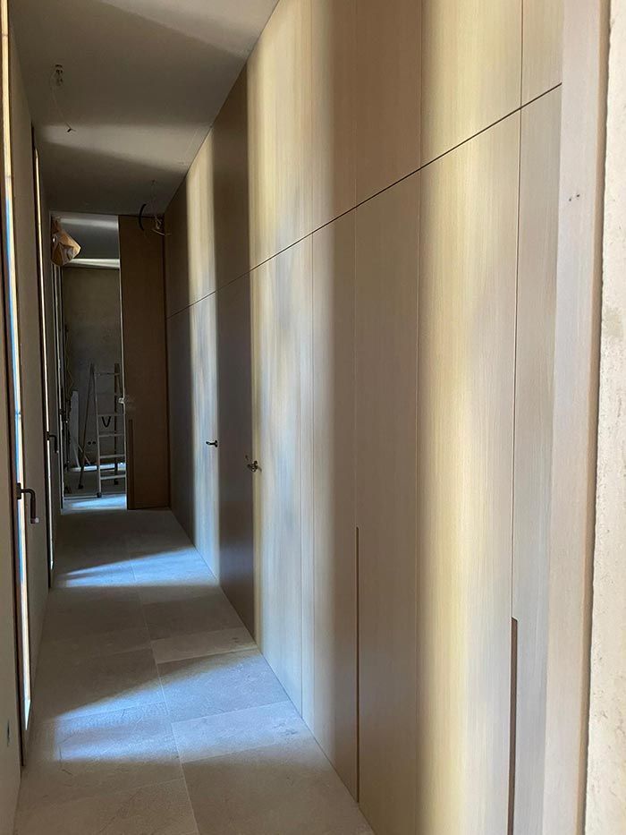 Pasillo estrecho con armarios empotrados de color claro a la derecha. Se ve otra puerta al final.