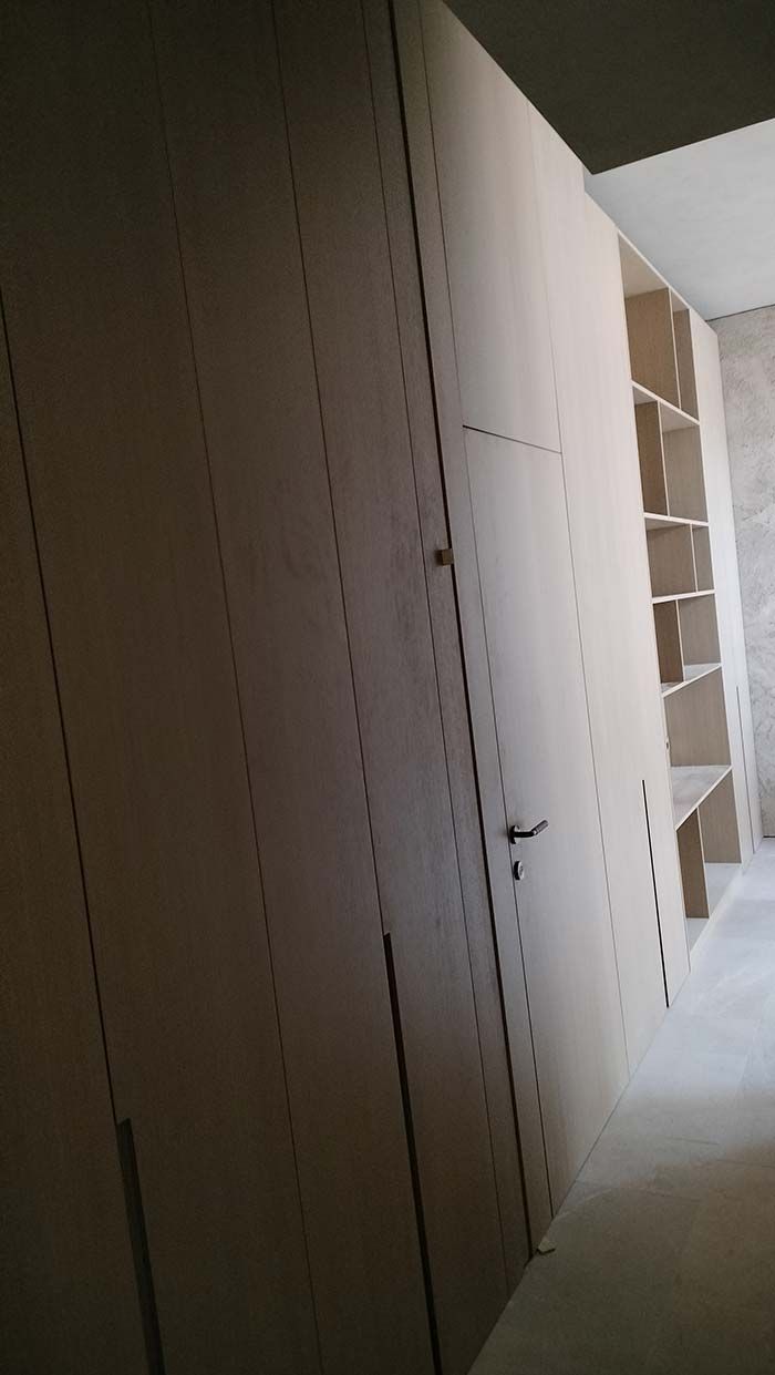 Armario empotrado de madera de color claro con puertas y estantes abiertos, apoyado sobre una pared de color claro.