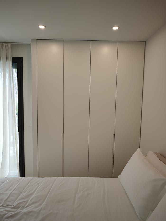 Dormitorio con cama blanca y armario. A la izquierda, una cortina transparente y una ventana.