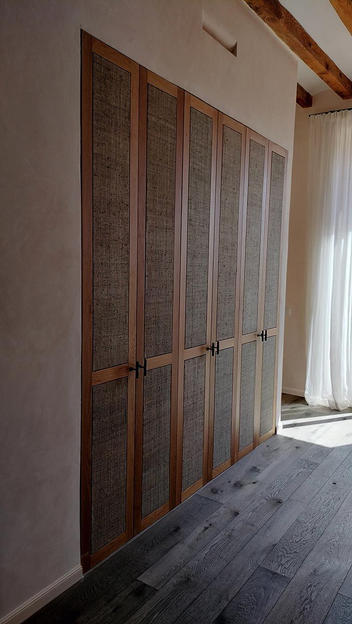 Puertas de armario de madera con paneles tejidos, junto a una ventana con cortinas transparentes.