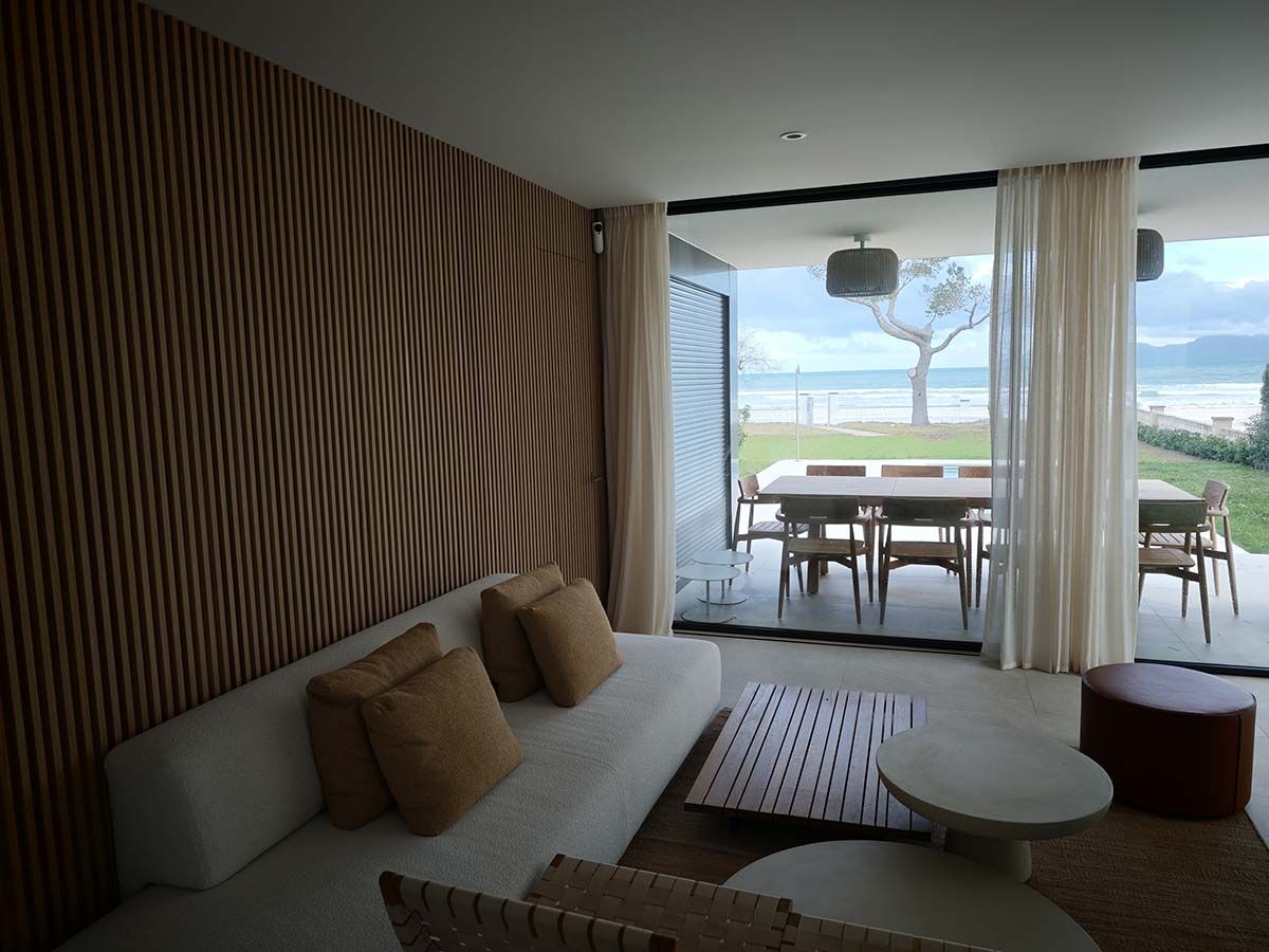 Sala de estar con pared de paneles de madera, sofá blanco y comedor al aire libre con vista al agua.