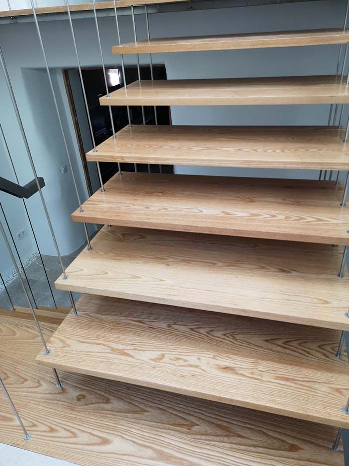 Escalera flotante de madera con barandillas de cable, que conduce hacia arriba.