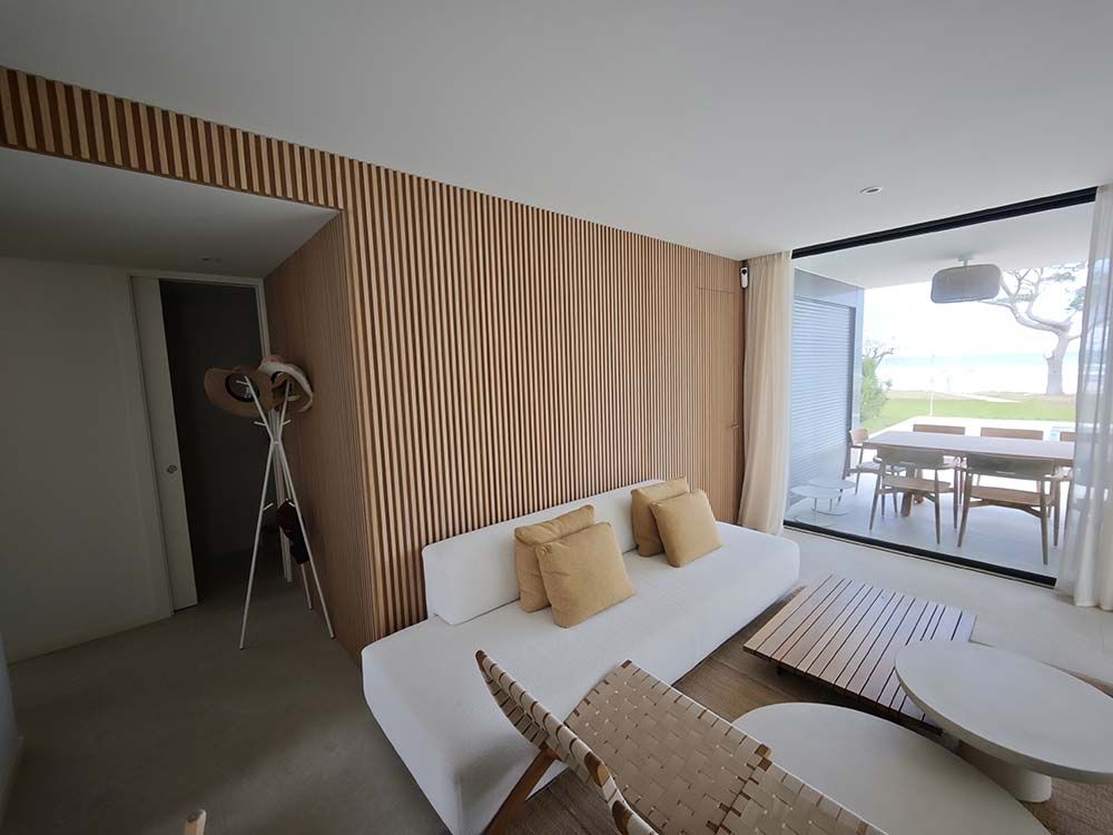 Moderna sala de estar con sofá blanco, pared con paneles de madera y abierta a un comedor al aire libre.