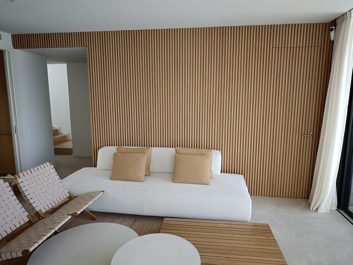 Sala de estar con pared de acento de madera, sofá blanco, sillas tejidas y mesas redondas.