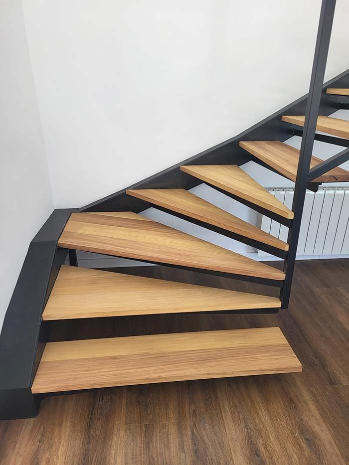 Escalera de madera con estructura de metal negro sobre una pared blanca y suelo imitación madera.