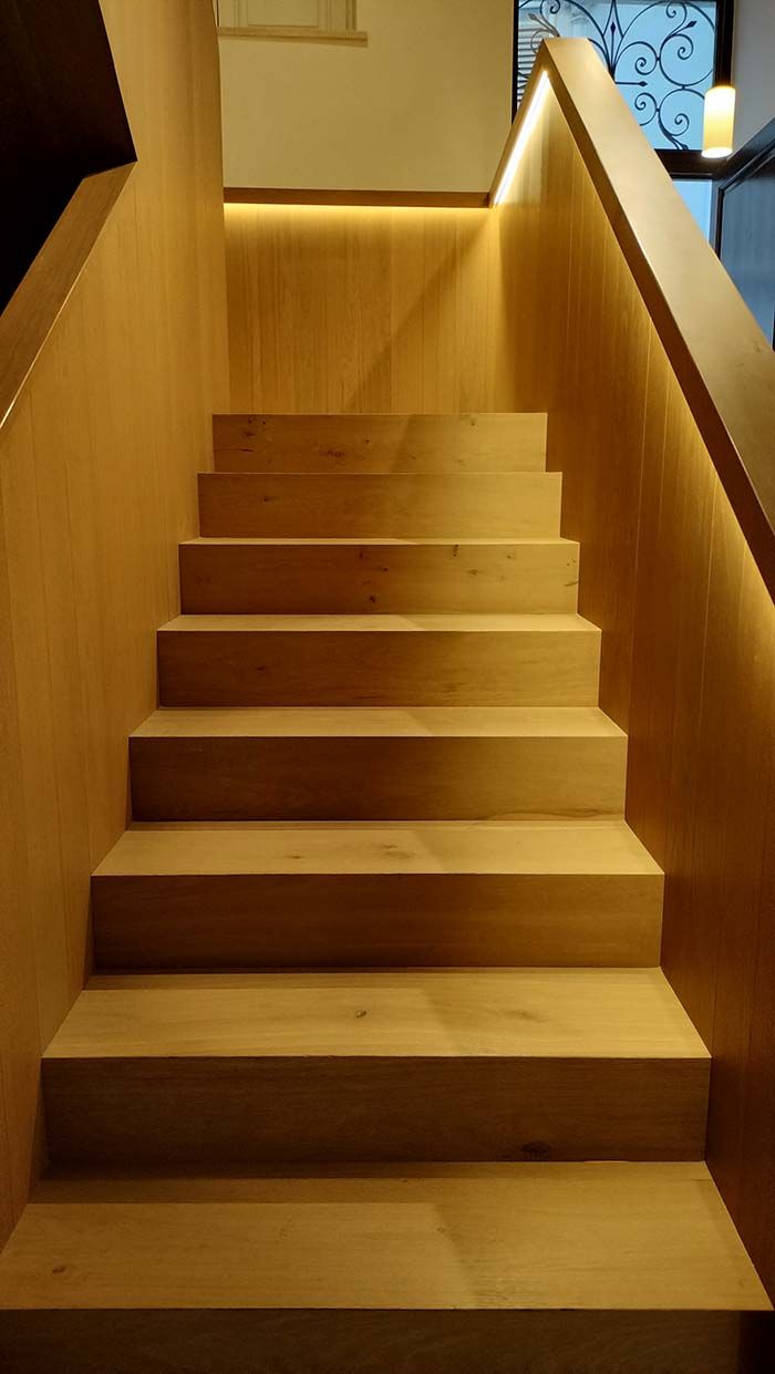 Escalera de madera con iluminación cálida a lo largo de la pared.