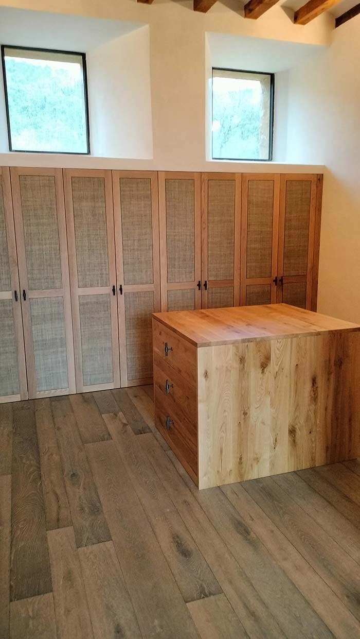 Muebles de madera y escritorio en una habitación con suelo de madera y pequeñas ventanas.
