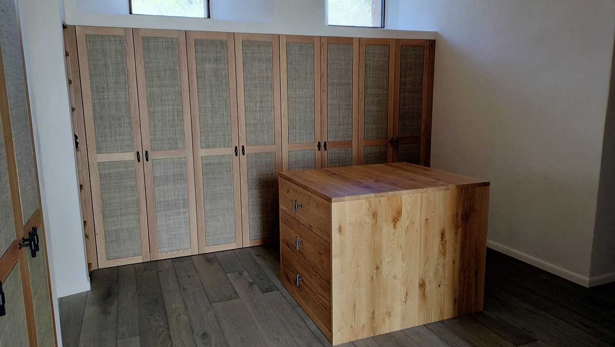 Armario y cómoda de madera en una habitación con suelos de madera y ventanas luminosas.