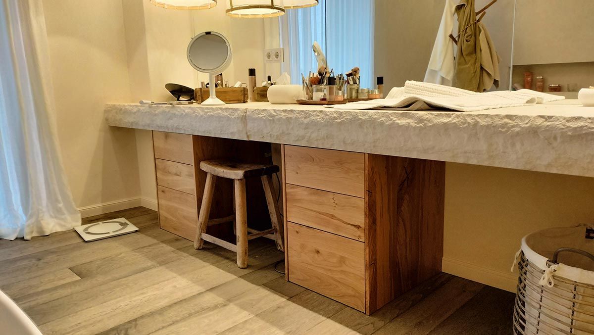 Área de tocador con taburete de madera, cajones y una encimera larga con espejo, luces y artículos de tocador.