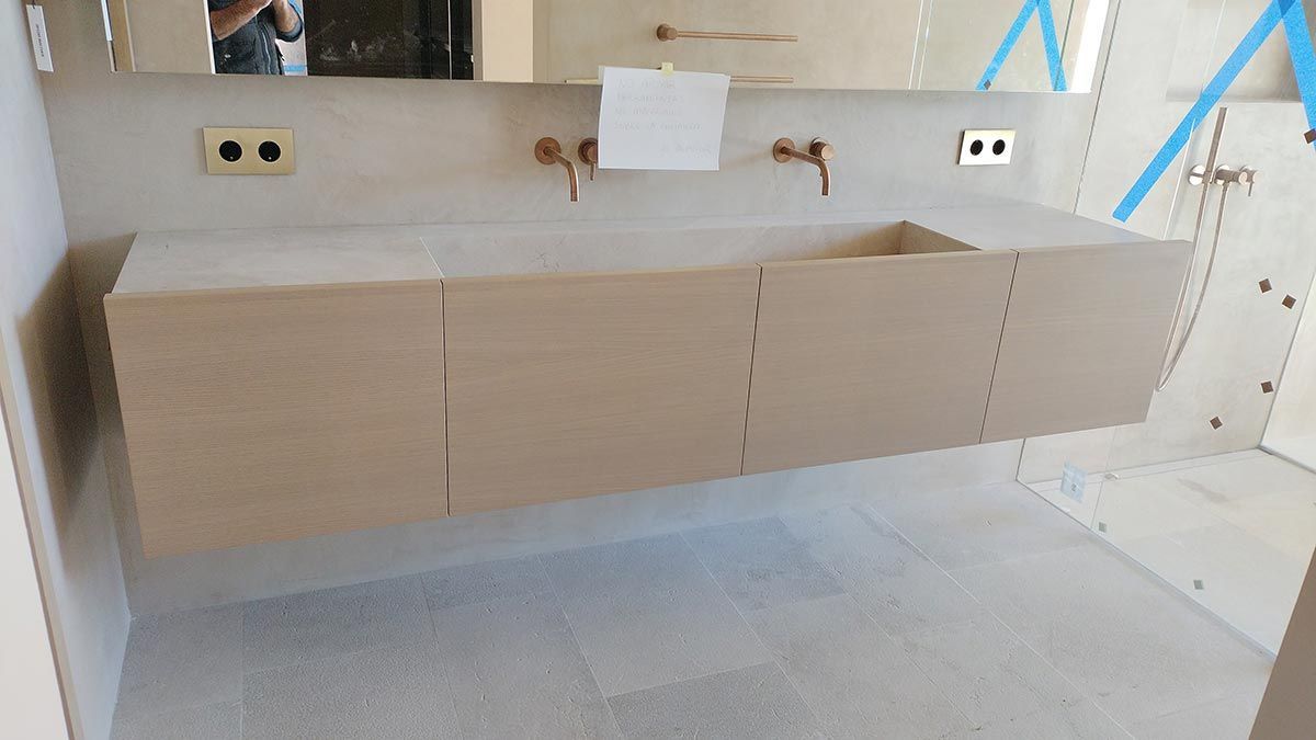 Baño en construcción: Tocador flotante color claro con lavabo, grifería de cobre, espejo y dos enchufes eléctricos.