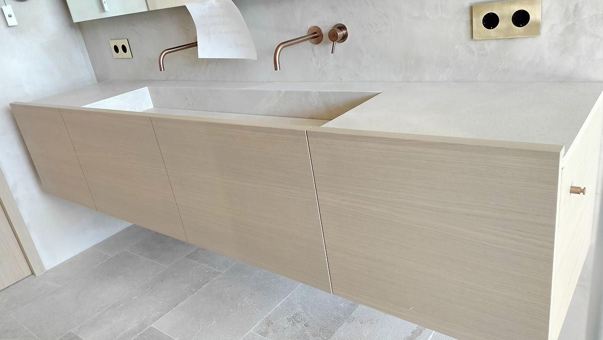 Tocador flotante de madera clara con dos griferías y lavabo integrado.