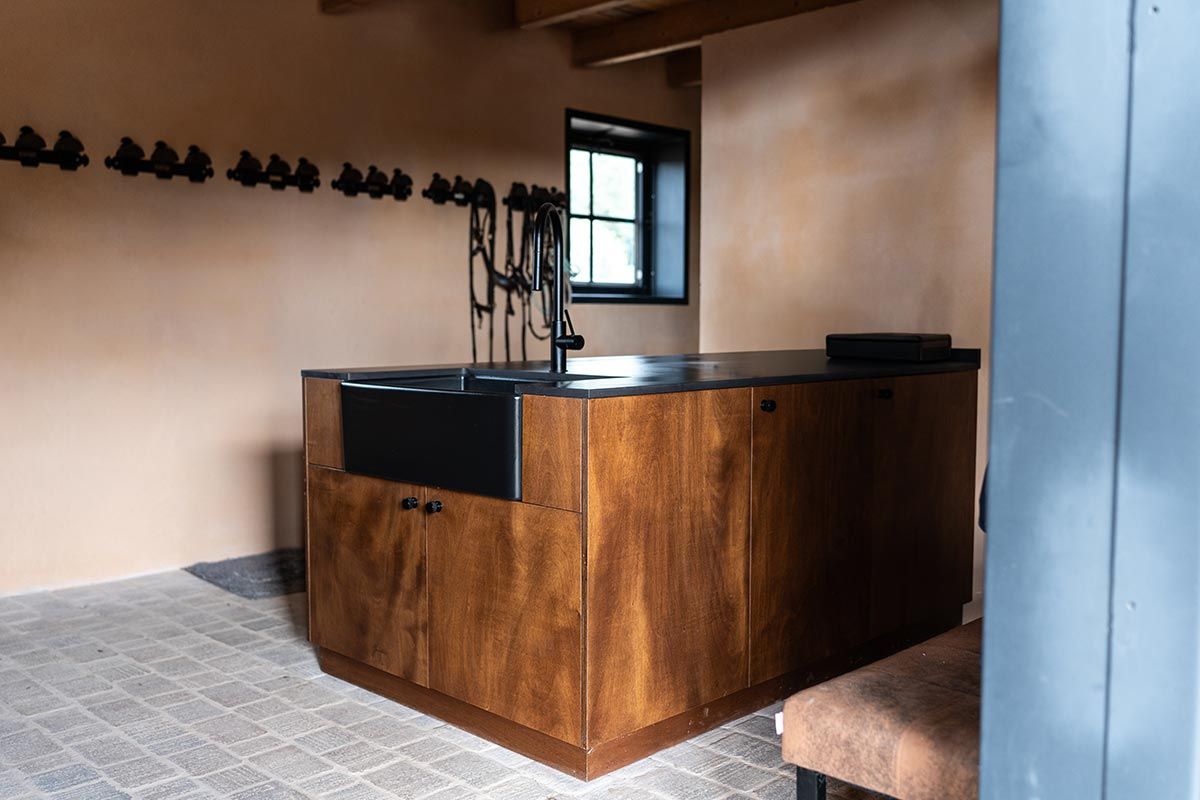 Barra de madera con barra y grifos oscuros, contra una pared color canela. Fregadero y ventana negros.